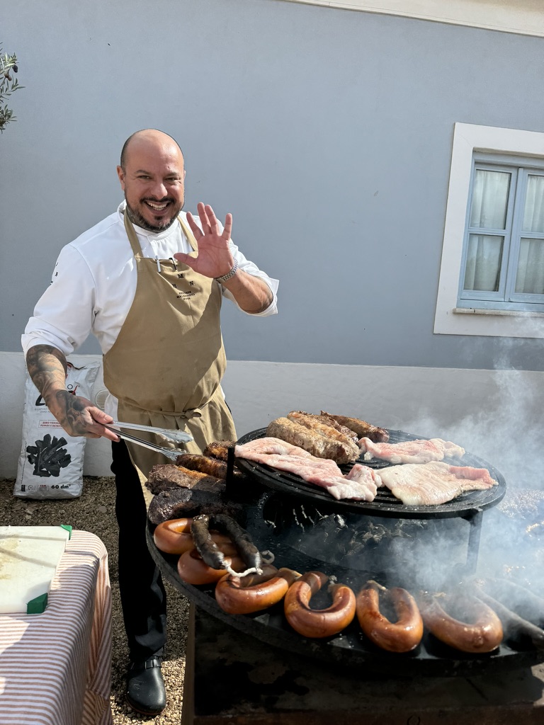 a man in an apron cooking meat on a grill with Annie B in Alentejo